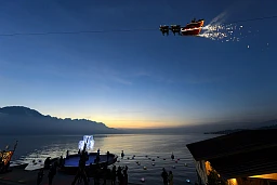 Der Weihnachtsmann winkt der Menge von seinem fliegenden Schlitten, der von Rentieren gezogen wird, über den Genfer See und in Der Weihnachtsmann winkt der Menge von seinem fliegenden Schlitten, der von Rentieren gezogen wird, über den Genfer See und in