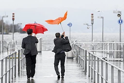 Two passersby try to protect themselves from the rain with their umbrellas on Friday, November 20, 2015, on the jetty at Buerkiplatz in Zurich. Heavy rainfall is expected next weekend. (KEYSTONE/Anthony Anex)