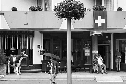 Suisse. Canton de Berne. Interlaken. Scène de la vie quotidienne un dimanche après-midi. Un couple, parapluie à la main, se promène sur le trottoir. Un touriste âgé est assis près d'une sculpture à l'entrée principale de l'hôtel. Une femme musulmane arabe, originaire du Moyen-Orient, est assise sur le balcon de sa chambre. 31.07.2016 © 2016 Didier Ruef Suisse. Canton de Berne. Interlaken. Scène de la vie quotidienne un dimanche après-midi. Un couple, parapluie à la main, se promène sur le trottoir. Un touriste âgé est assis près d'une sculpture à l'entrée principale de l'hôtel. Une femme musulmane arabe, originaire du Moyen-Orient, est assise sur le balcon de sa chambre. 31.07.2016 © 2016 Didier Ruef