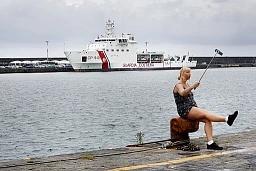 Italie, Sicile, Catane, le 4 octobre 2017. Le froid ne la contrarie même pas, elle prend la pose et se prend en photo. Derrière elle, le quai est fermé. Un navire a été mis en quarantaine. A son bord, 700 enfants, femmes et hommes repêchés au large de l'Italie après plusieurs jours de dérive , embarqués sur des canots de fortune pour fuir l'horreur. Cette image représente le contraste de ce monde. L'indifférence de certains gouvernement face à l'urgence.