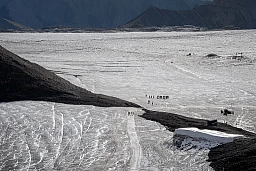 This picture taken on September 13, 2022 at Glacier 3000 resort above Les Diablerets shows tourists walking on the Tsanfleuron pass free of the ice that covered it for at least 2,000 years next to blankets covering snow from the last winter season to prevent it from melting. - The thick layer of ice that has covered a Swiss mountain pass between Scex Rouge glacier and Tsanfleuron glacier since at least the Roman era has melted away completely. Following a dry winter, the summer heatwaves hitting Europe have been catastrophic for the Alpine glaciers, which have been melting at an accelerated rate