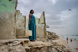 14. Juli 2024 – Magiette Gueye, 52, posiert am Meeresufer im Dorf Bargny in Senegal zwischen den Überresten der Häuser ihrer Nachbarn, die durch den steigenden Meeresspiegel zerstört wurden. Während Stürmen, besonders in der Regenzeit, dringt das Meer in das Dorf ein, erodiert den Strand und verschlingt nach und nach ganze Viertel. Magiette weisst, dass das Meer innerhalb eines oder zweier Jahre auch ihr Haus verschlingen wird, wodurch sie obdachlos werden wird.